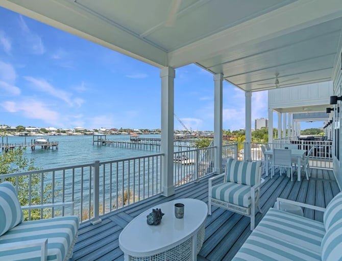 Covered waterfront deck with striped lounge chairs, white table, and views of turquoise water and distant docks